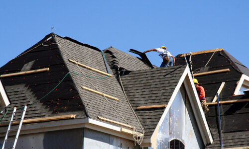 Construction workers putting shingles on the roof of a house.